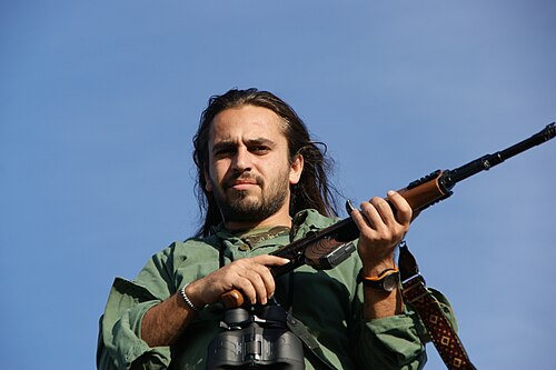 Airsoft player holding a rifle replica and binoculars outdoors